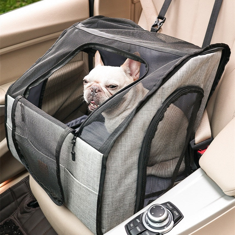 French bulldog sitting in a gray booster seat on a car passenger seat
